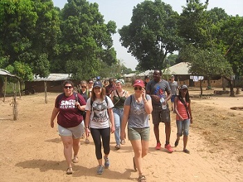 A group of twelve Saint Mary's students walk towards the camera as they pass through a rural village in The Gambia, West Africa, during a 2015 field course.