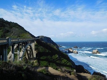 With the Pacific Ocean in the background, the morning sun casts a shadow of the Rocky Creek Bridge onto the cliffside below the Cabrillo Highway, north of Big Sur, California, USA.