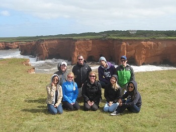 A group of nine Saint Mary's students pose for a picture in front of coastal red cliffs during a 2014 field course to Les Îles-de-la-Madeleine, Québec.